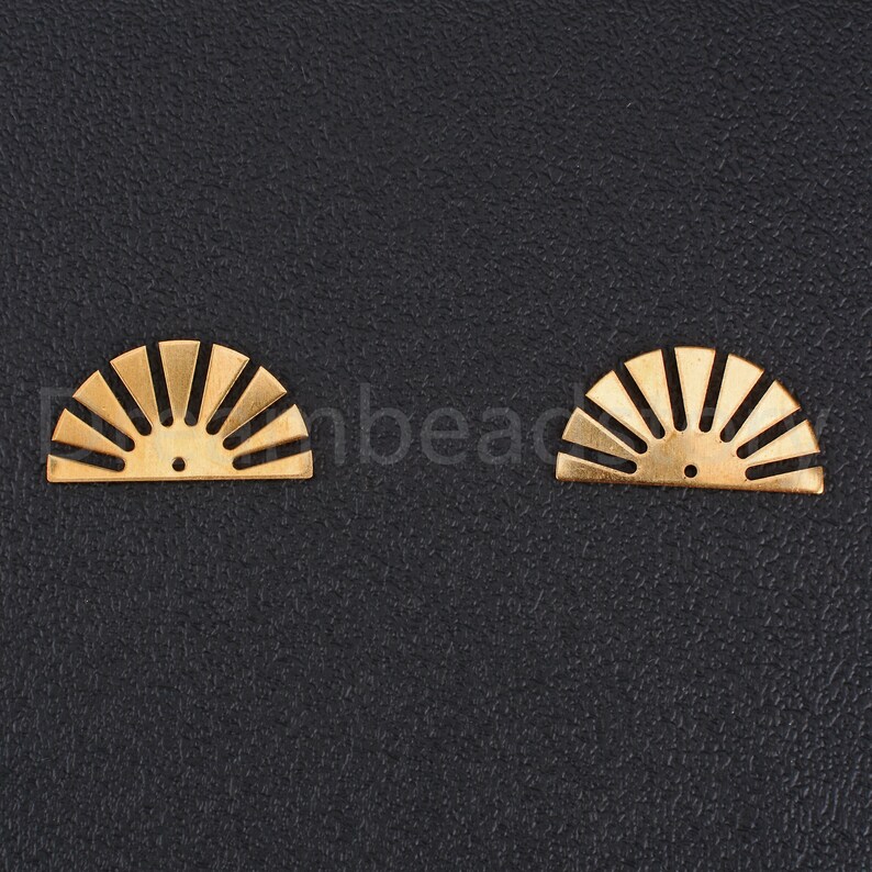 May include: Two gold-colored metal sunburst shapes with a hole in the center. The shapes are on a black background.