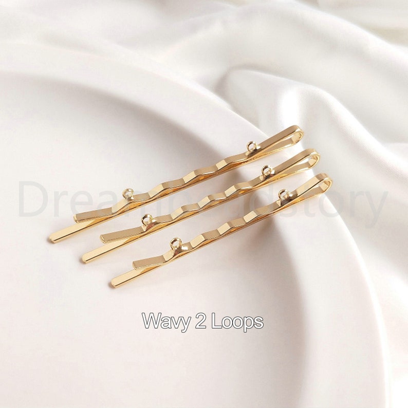 May include: Three gold wavy hair clips with two loops at the end of each clip. The clips are arranged in a row, with the top clip slightly offset from the other two.