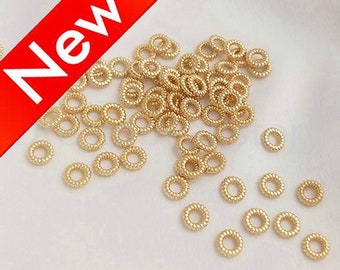 May include: A large quantity of gold-colored metal jump rings. The rings are small and have a coiled design.