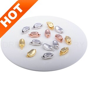 May include: Assortment of silver, gold, and rose gold lobster clasps for jewelry making. The clasps are in various positions on a white plate.