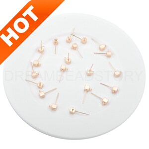 May include: A collection of 15 gold-toned square earring posts with a loop on the top. The earring posts are scattered on a white surface.