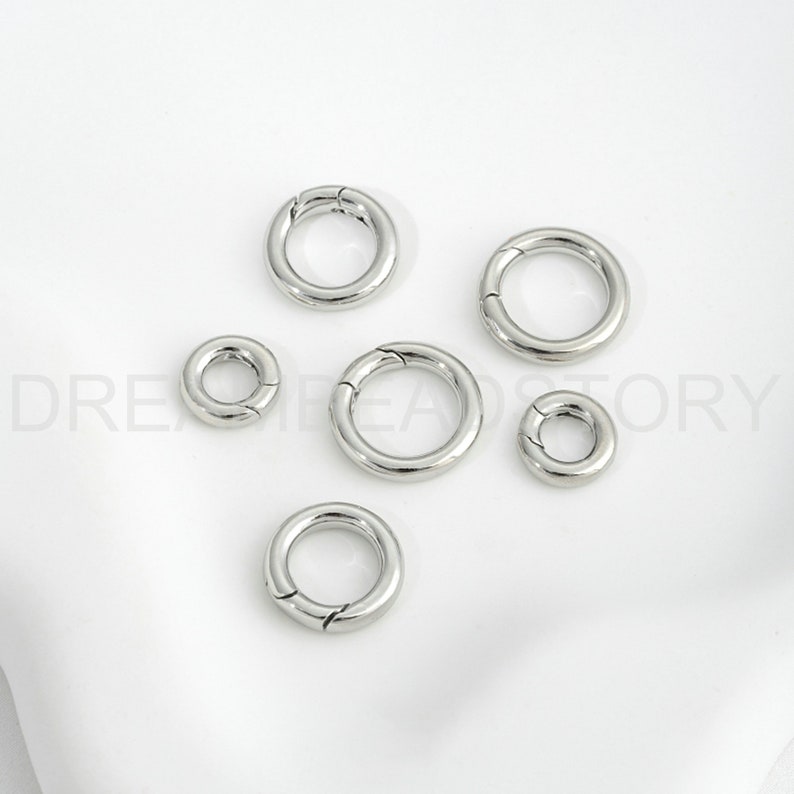 Op de afbeelding: Vijf zilveren metalen springringen in verschillende maten. De ringen zijn open en hebben een gladde afwerking.