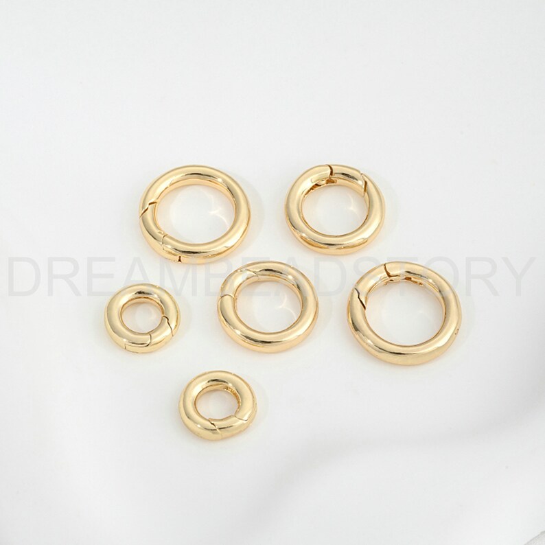 Op de afbeelding: Vijf goudkleurige metalen springringen in verschillende maten. De ringen zijn open en hebben een gladde afwerking.