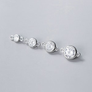 May include: Four silver connector charms with clear round cubic zirconia stones. The charms have two loops on each side for attaching to jewelry.