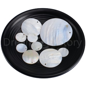 Peut inclure: Une collection de cercles de nacre blanche avec des trous au centre. Les coquillages sont disposés sur une assiette noire.