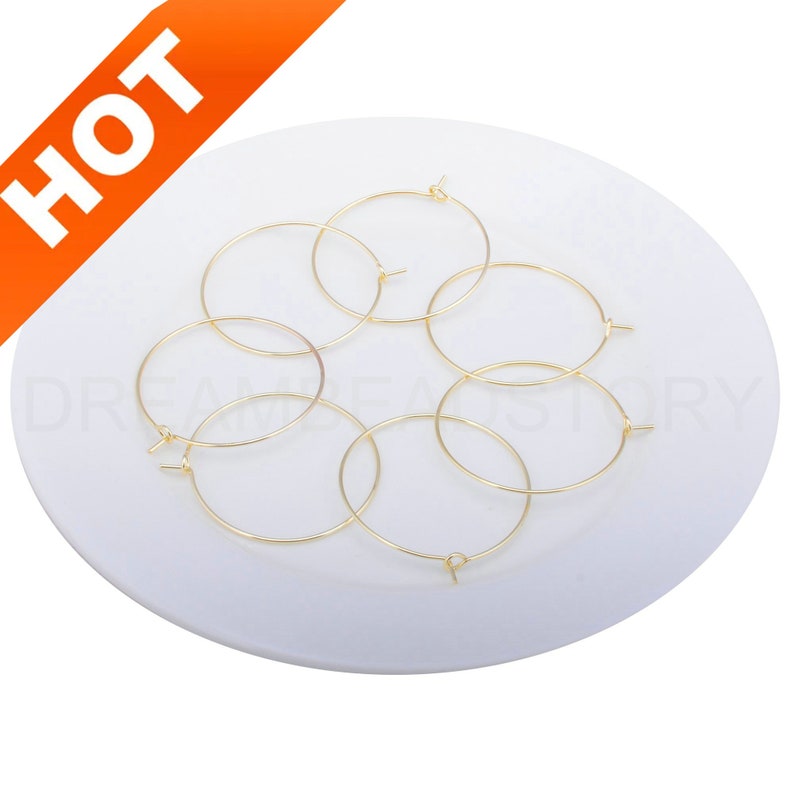 May include: Six gold-coloured hoop earrings on a white plate. The hoops are all the same size and have a simple, circular design.