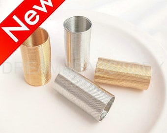 May include: Four spools of wire, two gold and two silver, are arranged on a white surface. The spools are made of thin metal wire that is tightly wound into a coil.