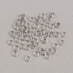 May include: A large quantity of silver jump rings, scattered on a gray surface.