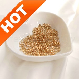 May include: A white heart-shaped dish filled with a large quantity of small, gold-colored jump rings.
