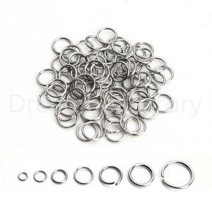 May include: A large pile of silver jump rings, a common jewelry making supply.  The rings are arranged in a random pattern.  A row of seven jump rings of different sizes is shown below the pile.