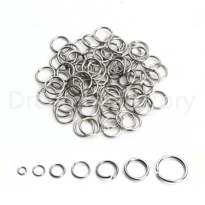 May include: A large pile of silver jump rings, a common jewelry making supply.  The rings are arranged in a random pattern.  A row of seven jump rings of different sizes is shown below the pile.