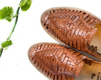 May include: A pair of brown leather sandals with a woven design. The sandals have a slip-on style and are made in Mexico.