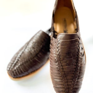 May include: A pair of brown leather sandals with a woven design. The sandals are made of a soft, supple leather and have a comfortable fit.