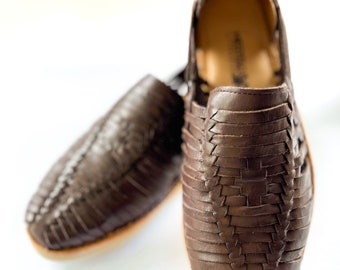 May include: A pair of brown leather sandals with a woven design. The sandals are made of a soft, supple leather and have a comfortable fit.