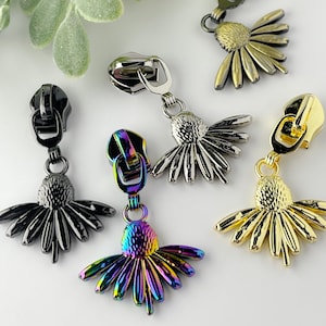May include: Five zipper pulls with daisy-shaped charms. The charms are in black, silver, gold, and iridescent colors.