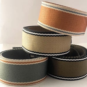 May include: Four rolls of striped webbing in different colors. The webbing is woven with black, white, and a third color. The colors are tan, orange, green, and gray.