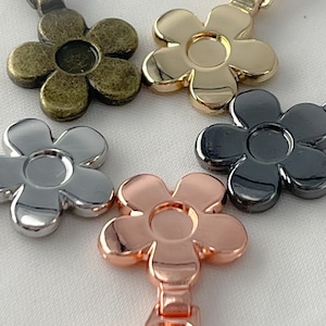 May include: Close-up of five flower-shaped zipper pulls in various metallic finishes: antique brass, gold, silver, gunmetal, and rose gold. Each pull has a central circular indentation and a matching zipper attachment.