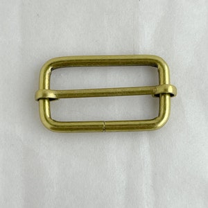 May include: A gold-toned metal buckle with a rectangular shape and a smooth finish.