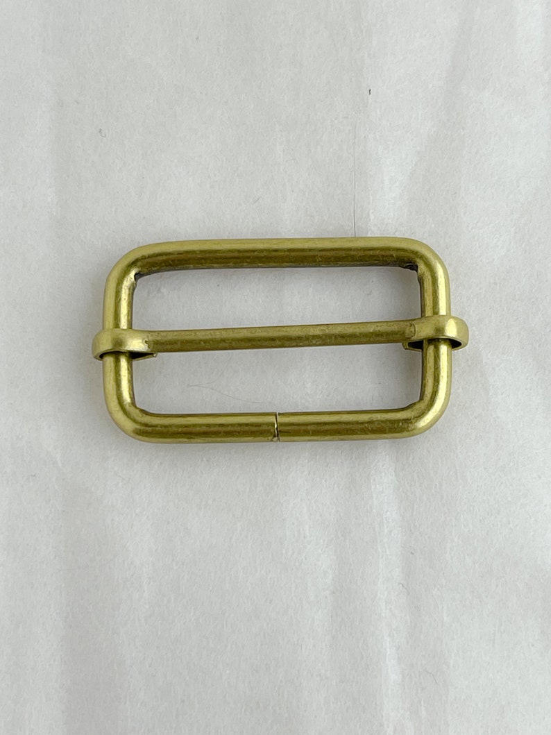 May include: A gold-toned metal buckle with a rectangular shape and a smooth finish.