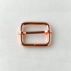May include: A rose gold metal buckle for a strap or belt.