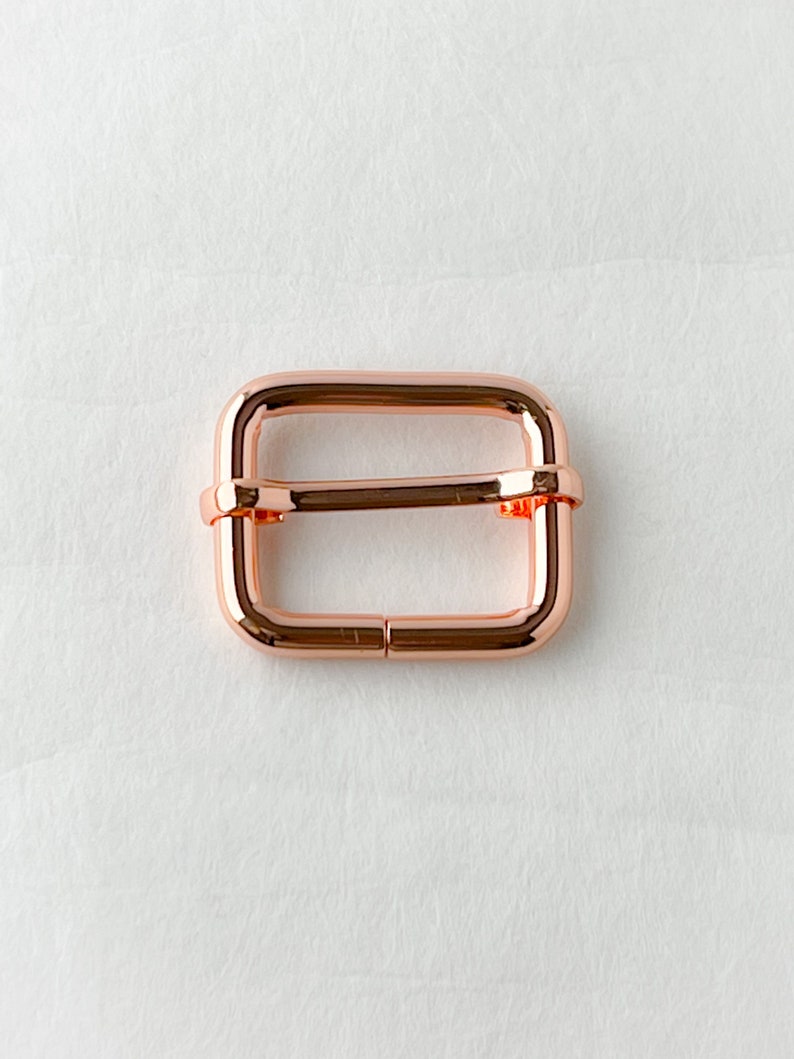 May include: A rose gold metal buckle for a strap or belt.