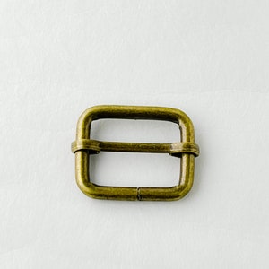May include: A gold-toned metal buckle with a rectangular shape. The buckle has a smooth, polished finish.