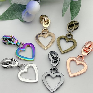 May include: Assortment of six zipper pulls with heart-shaped charms. The charms are in various colors, including gold, silver, rose gold, and iridescent.