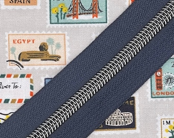 May include: A navy blue zipper with a silver metal coil. The zipper is lying on a fabric background with a pattern of colorful postage stamps.