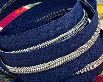 May include: A coiled navy blue zipper with a silver metal zipper pull. The zipper is made of a durable fabric and features a continuous coil design. The background shows a colorful floral pattern.
