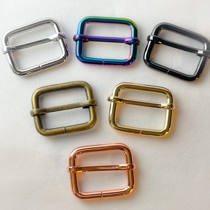 May include: Six different metal slider buckles in various finishes: silver, rainbow, black, brass, gold, and rose gold. The buckles are all the same size and shape, with a rectangular frame and a center bar.