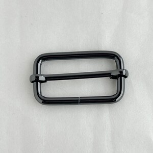 May include: A black metal buckle with a rectangular shape and a smooth finish.