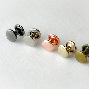 May include: Five metal rivets in different colors: black, silver, copper, gold, and brass. The rivets are round and have a flat head.