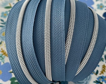 May include: A close-up of a roll of blue zipper tape with silver teeth. The zipper tape is folded in a spiral shape.