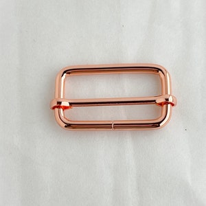 May include: A rose gold metal slider buckle for a strap or belt.