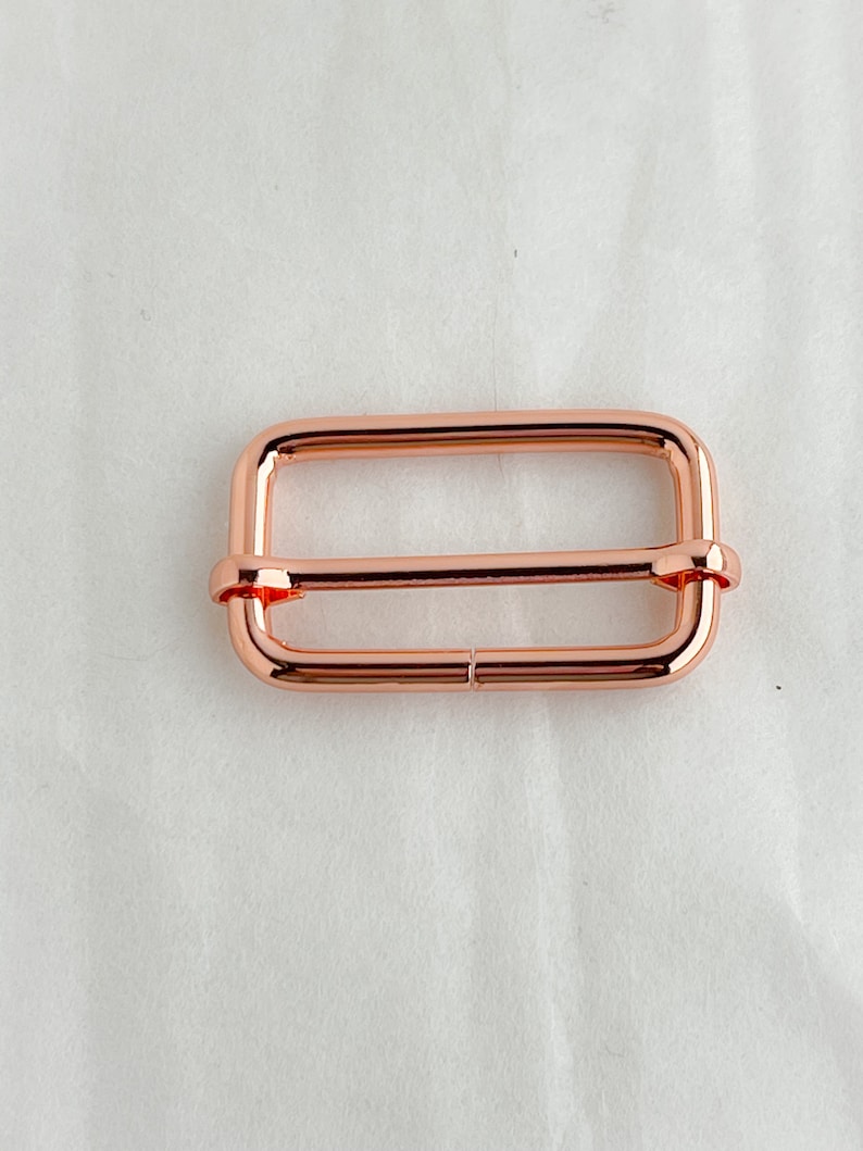 May include: A rose gold metal slider buckle for a strap or belt.