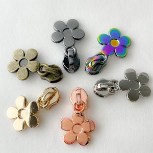 May include: Assortment of six flower-shaped zipper pulls in various colors and finishes, including black, silver, gold, and iridescent.
