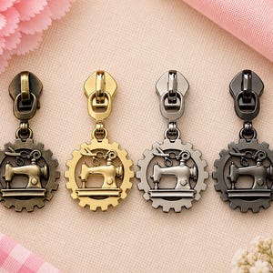 May include: Four metal zipper pulls arranged in a row, each featuring a circular gear-shaped frame with a sewing machine and scissors motif. The pulls are finished in antique bronze, bright gold, silver, and gunmetal gray metallic tones.
