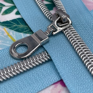 May include: Close-up of a silver zipper pull with a blue zipper tape and a floral fabric background.
