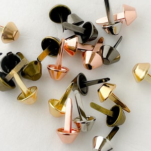 May include: Assortment of metal cone-shaped rivets in various colors, including gold, silver, copper, and black. The rivets have a pointed end and a flat base.