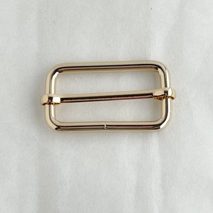 May include: Gold metal buckle with a rectangular shape and a smooth finish.