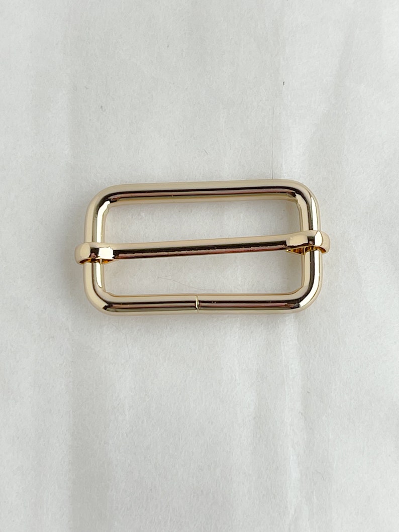 May include: Gold metal buckle with a rectangular shape and a smooth finish.