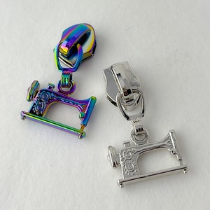 May include: Two zipper pulls with sewing machine charms. One pull is silver and the other is iridescent.