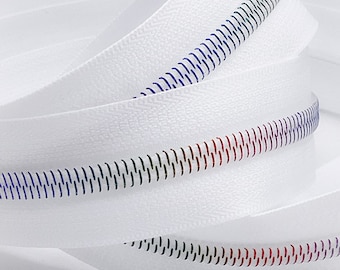 May include: White zipper tape with a blue, black, and red coil zipper. The zipper tape is folded and coiled.