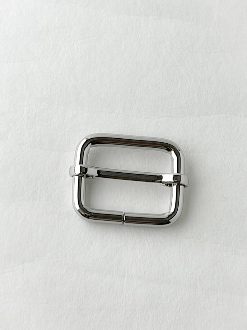 May include: A silver metal slider buckle for a strap or belt.