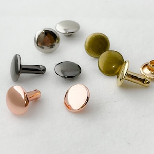May include: Assortment of metal rivets in various colors, including gold, silver, black, and copper. The rivets have a round head and a post for attaching to fabric or leather.