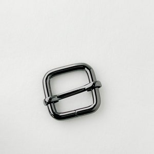 Op de afbeelding: Een zwarte vierkante metalen gesp voor een riem of band.