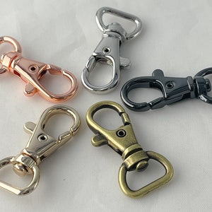 May include: Five metal swivel clasps in different finishes: rose gold, silver, black, and antique brass. Each clasp has a D-ring and a hook.