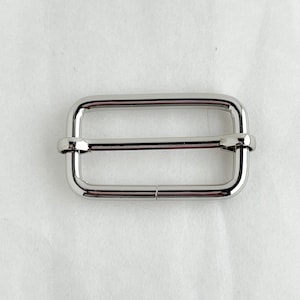 May include: Silver metal buckle with a rectangular shape and two holes on each side.