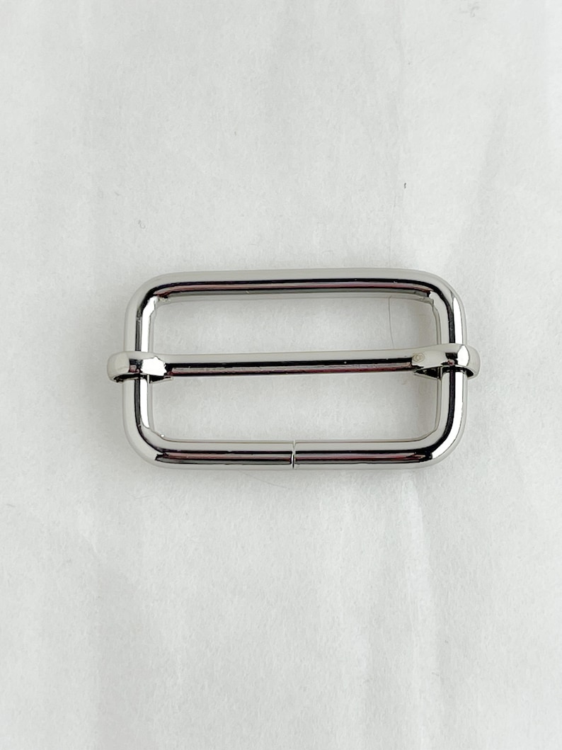 May include: Silver metal buckle with a rectangular shape and two holes on each side.