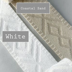 K&ouml;nnte beinhalten: Zwei Rollen gewebtes Stoffband mit einem geometrischen Rautenmuster. Eine Rolle ist mit White beschriftet und ist strahlend wei&szlig;, w&auml;hrend die andere mit Coastal Sand beschriftet ist und eine hellbeige Farbe hat. Beide B&auml;nder haben ein strukturiertes Gewebe.